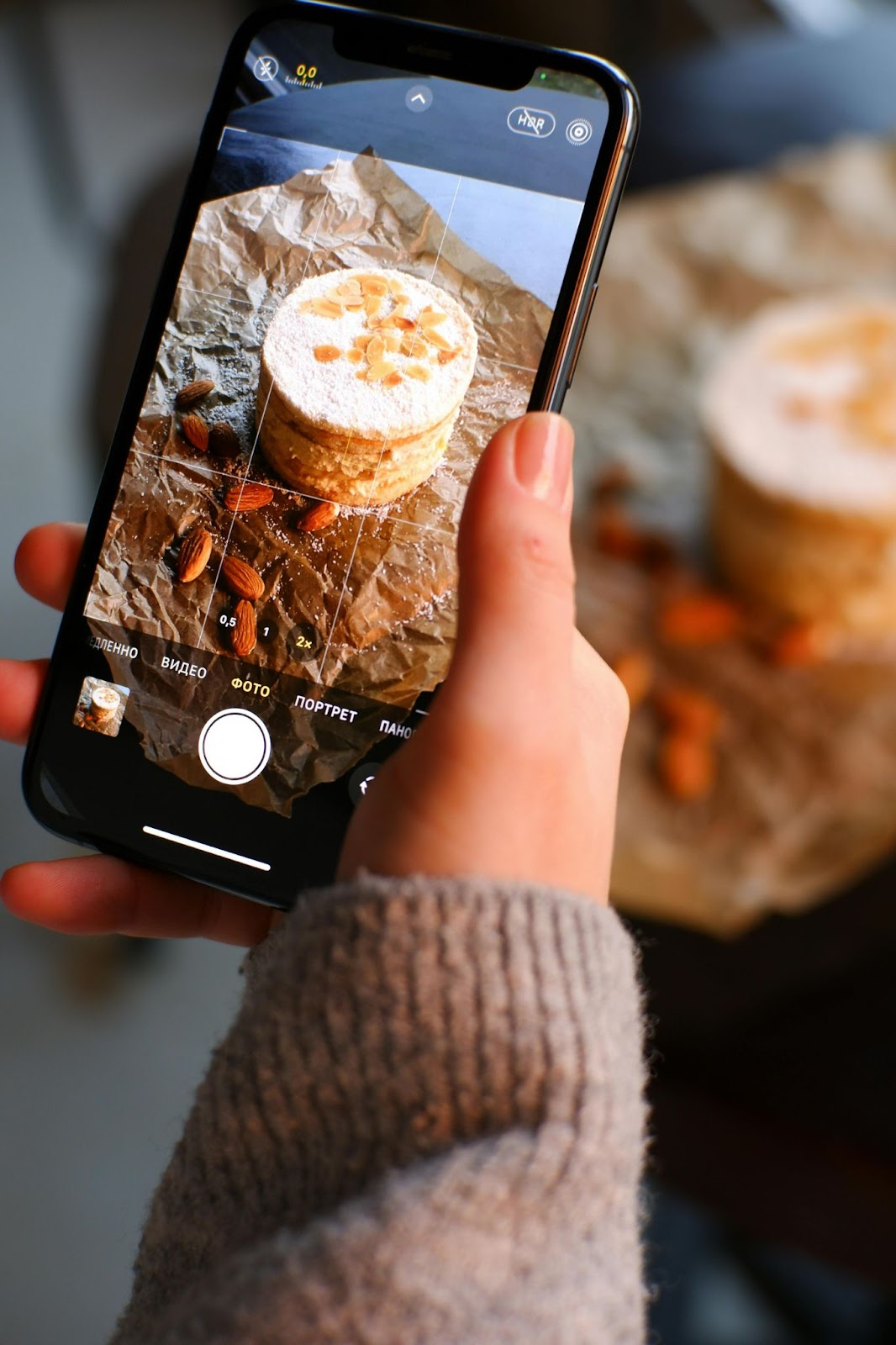 A content creator photographing a dessert with almonds on a smartphone screen.